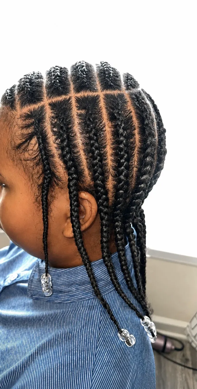 Child's straight-back cornrows in natural black finished with clear beads on the ends, side view